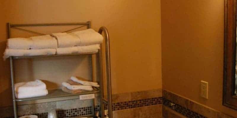 A bathroom with a shelf filled with towels and a mirror.