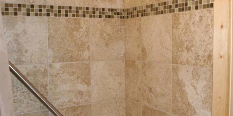 A bathroom with tiled walls and a stainless steel railing.