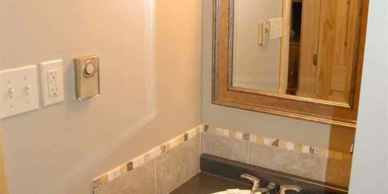 A bathroom with a sink , mirror and light switches.