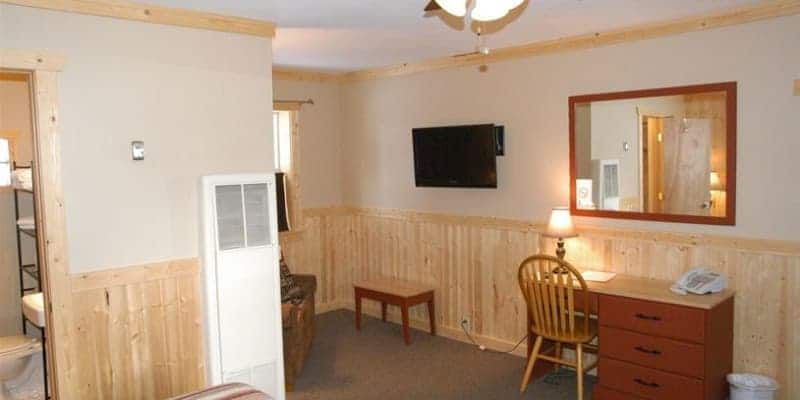 A hotel room with a desk , chair , television and mirror.