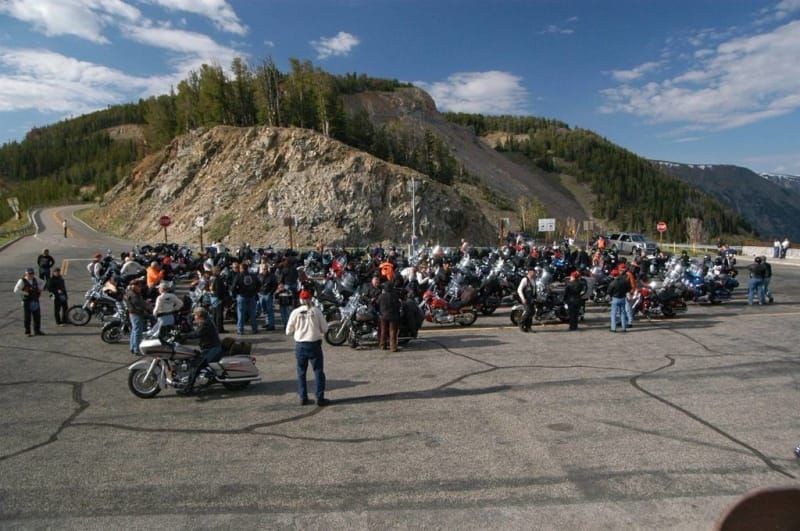 A large group of people are standing around motorcycles in a parking lot