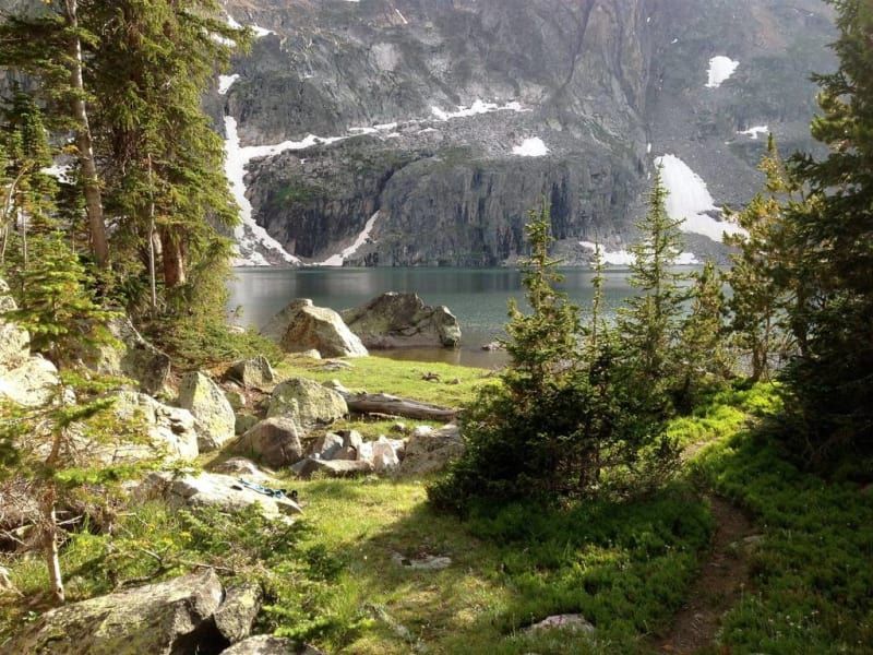 A lake surrounded by trees and rocks with mountains in the background
