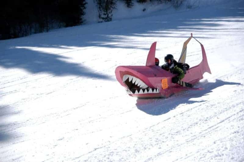A person is riding a pink shark sled in the snow.