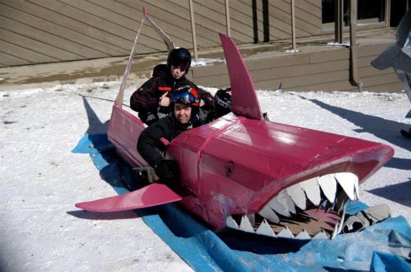 Two people are riding in a pink shark sled