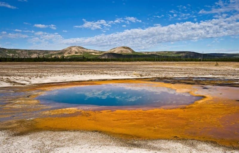 A small pool of water in the middle of a desert with mountains in the background.