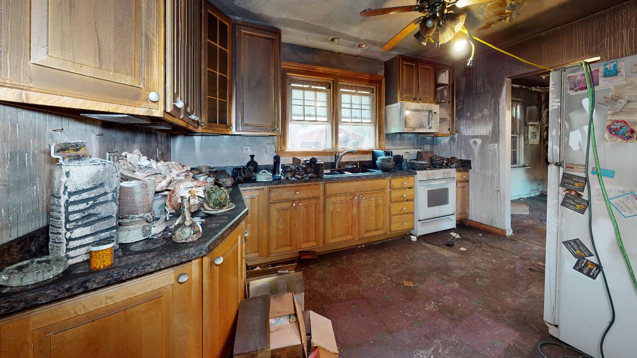 A kitchen with wooden cabinets , a refrigerator , a stove , and a ceiling fan.