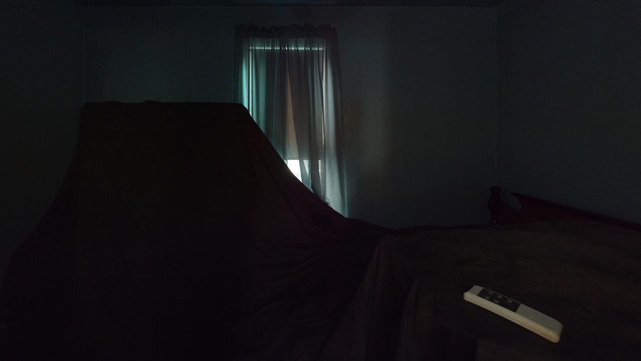 A remote control is sitting on a couch in a dark room next to a window.