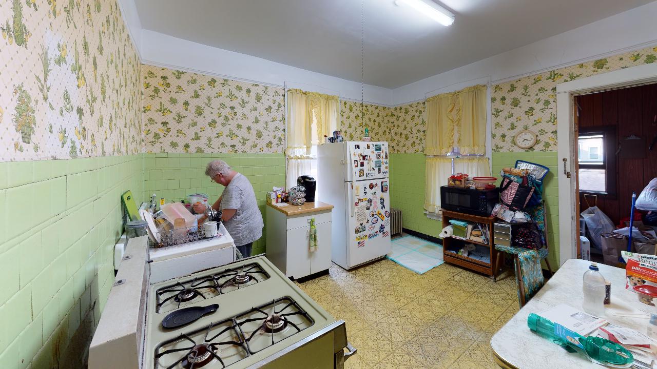 A man is cooking in a kitchen with a stove and a refrigerator.