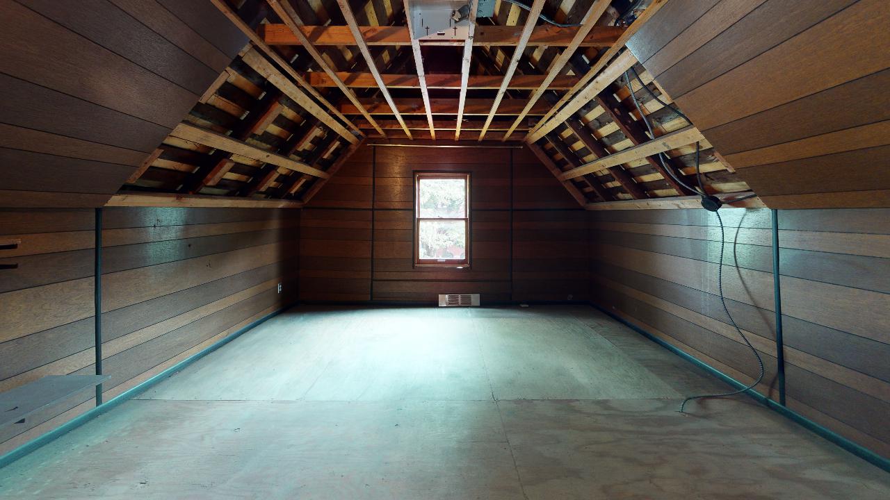 An empty attic with wooden walls and a window.
