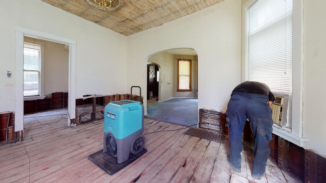 A man is working on a wooden floor in an empty room.