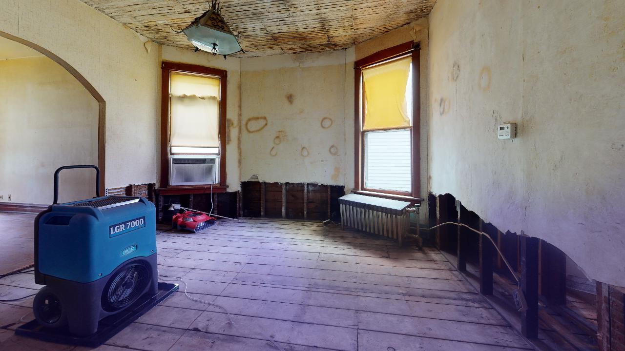 An empty room with a fan on the floor and a window.