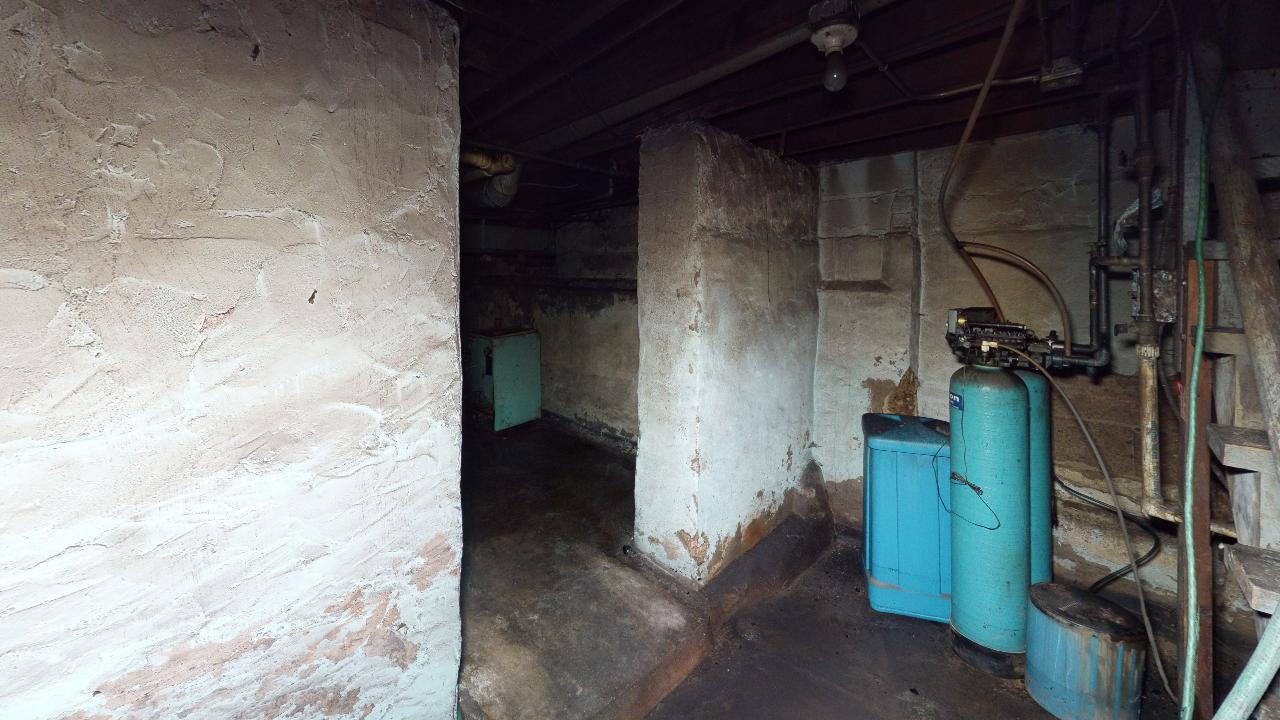 A dirty basement with a lot of pipes and a blue tank.