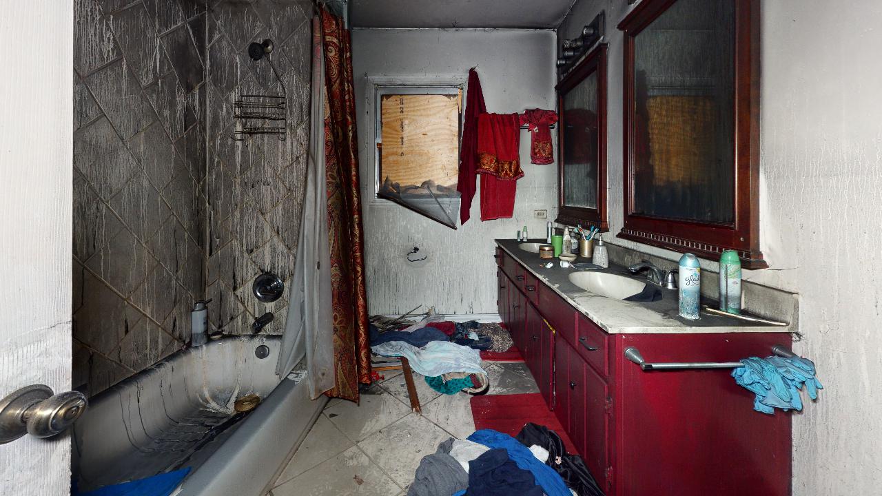 A bathroom with a bathtub , sinks , mirrors and clothes on the floor.