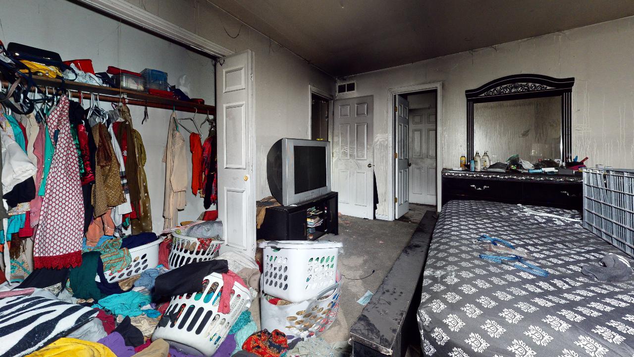 A bedroom with a bed , dresser , television , and closet filled with clothes.