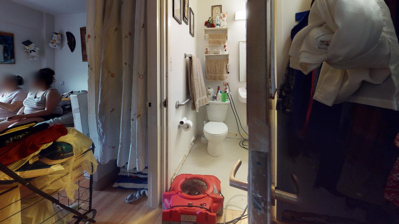 A woman is sitting on a bed next to a toilet in a bathroom.