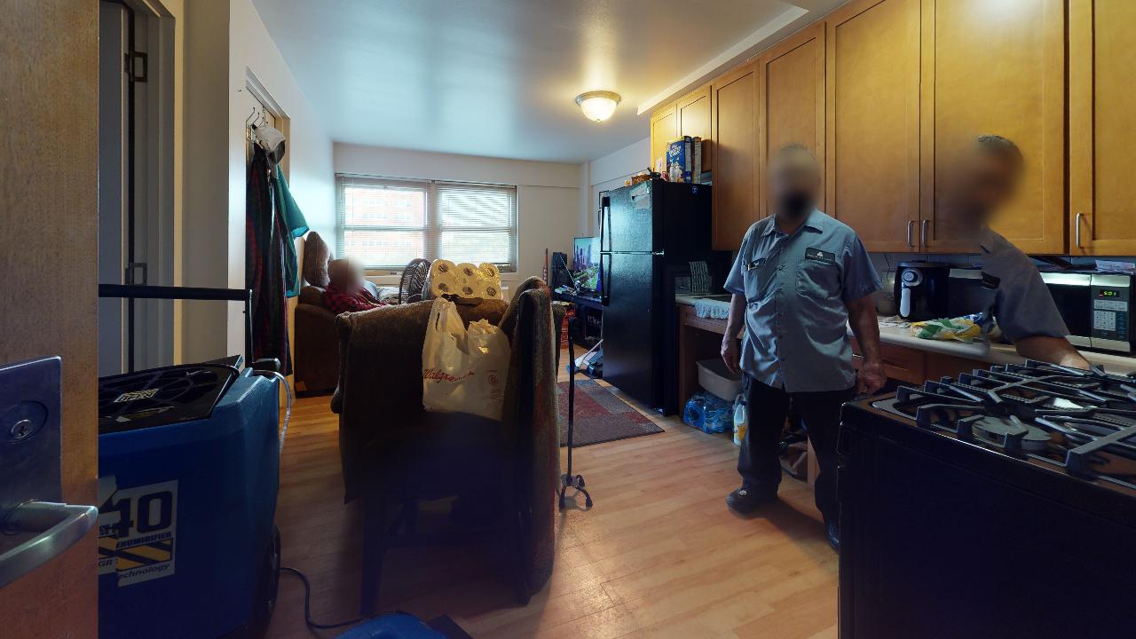 A couple of men are standing in a living room and kitchen.