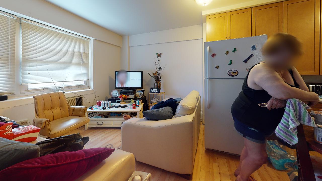 A woman is standing in a living room next to a refrigerator.