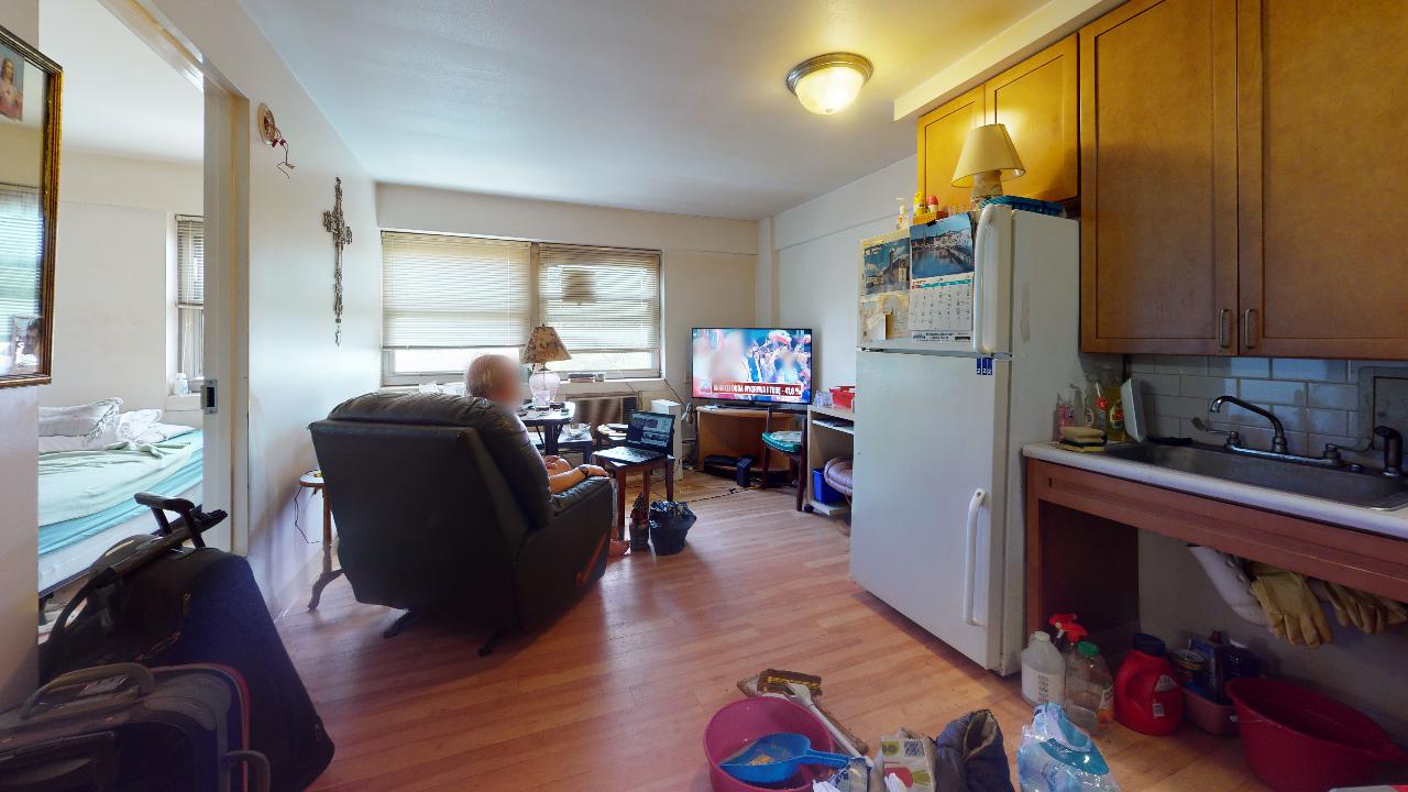 A man is sitting in a chair in a living room next to a refrigerator.