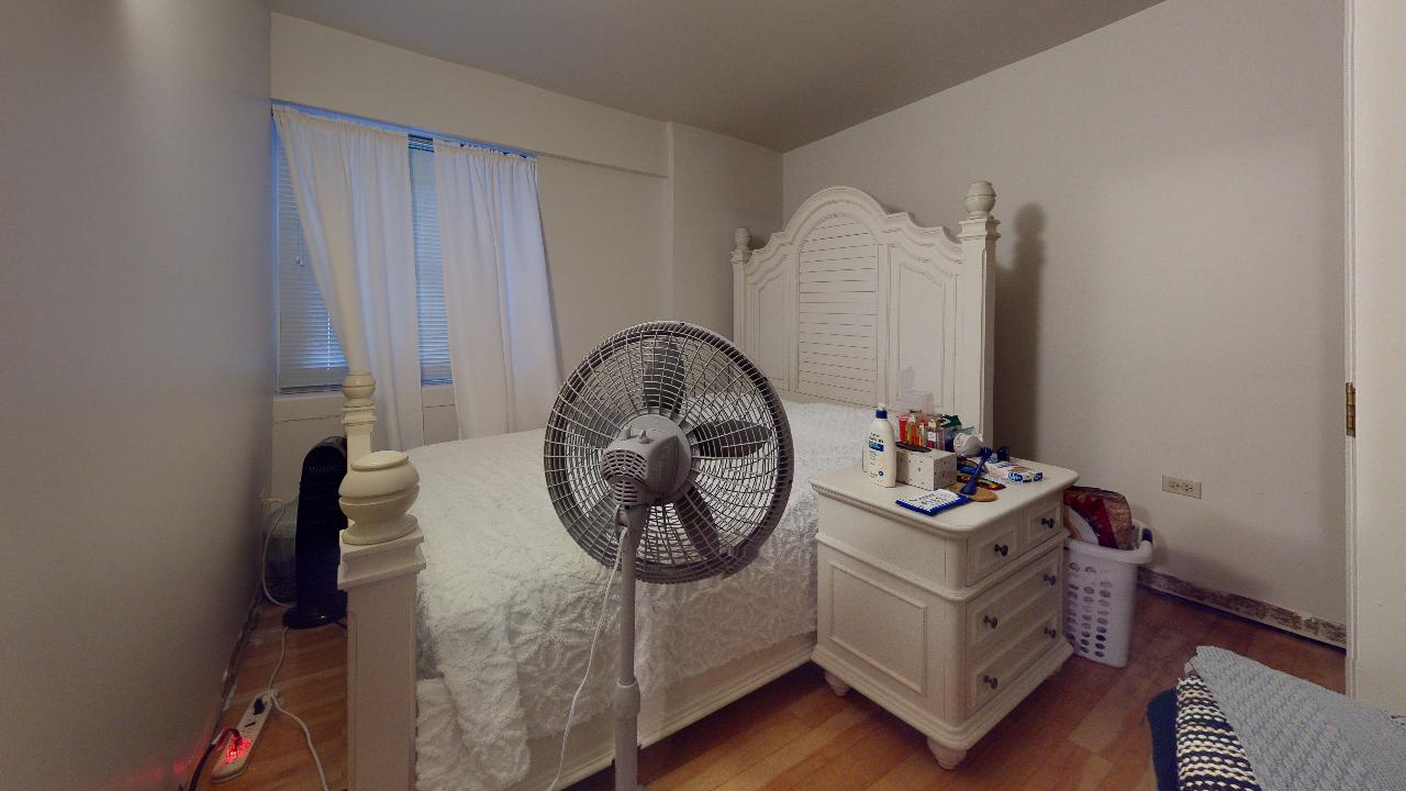 A bedroom with a bed , nightstand , and fan.
