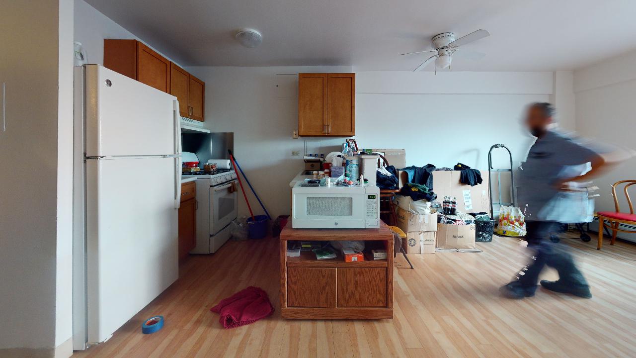 A man is walking through a living room filled with boxes and a refrigerator.