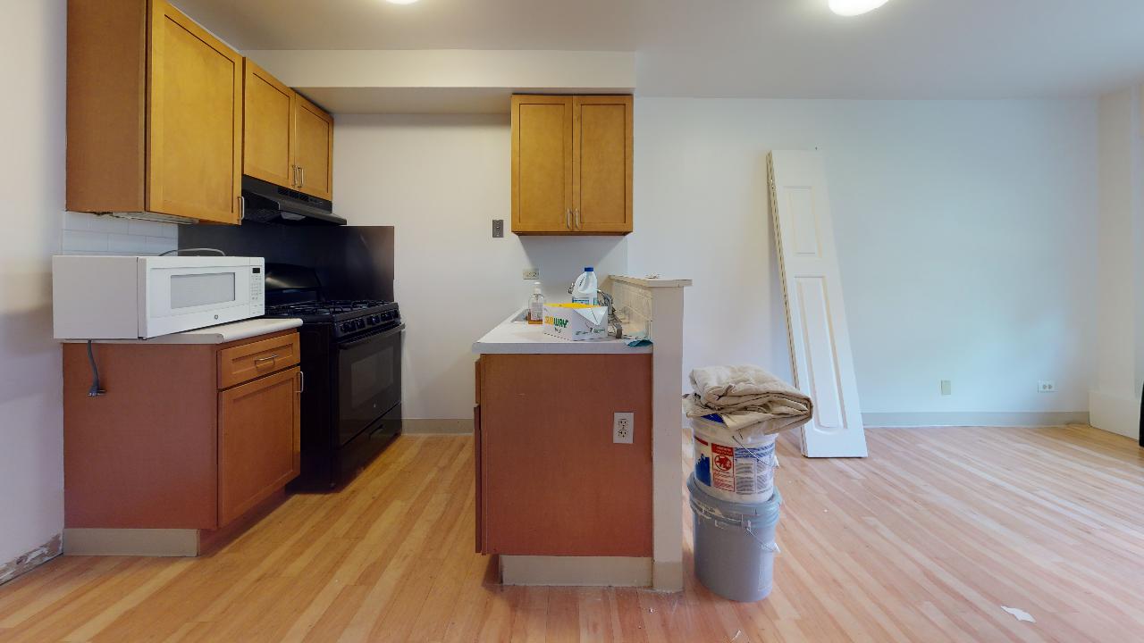 A kitchen with wooden cabinets , a stove , a microwave , and a trash can.