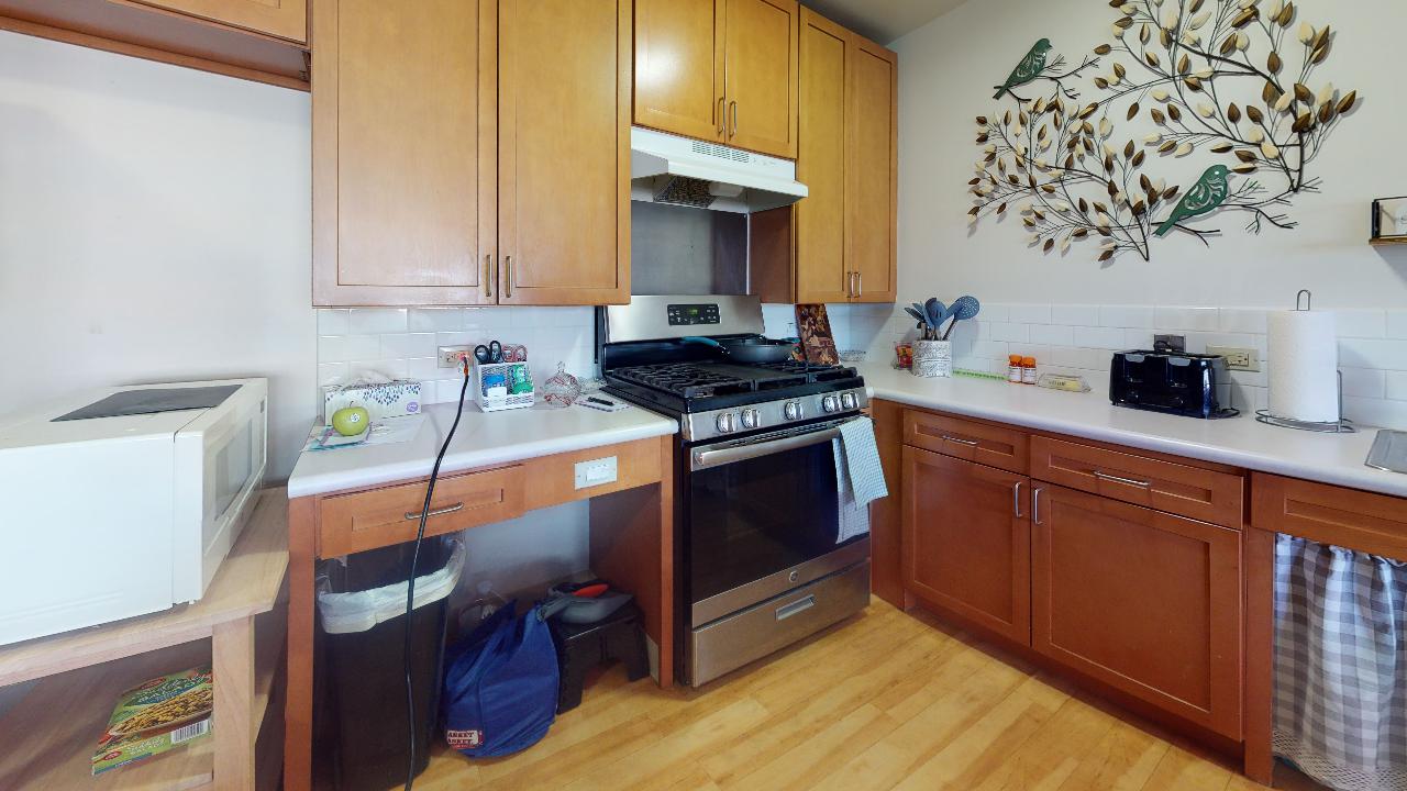 A kitchen with wooden cabinets , stainless steel appliances , a stove and a microwave.