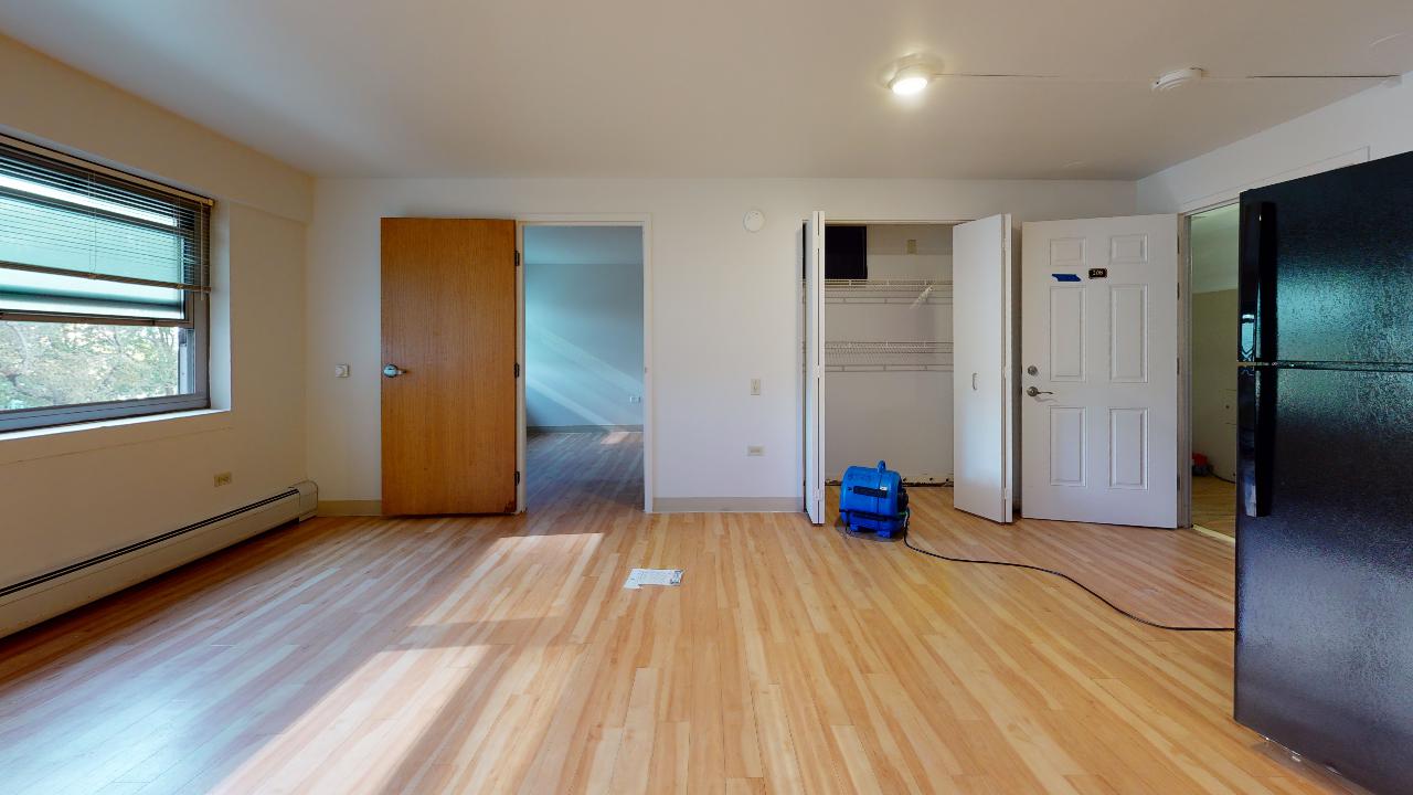 An empty living room with hardwood floors and a black refrigerator.