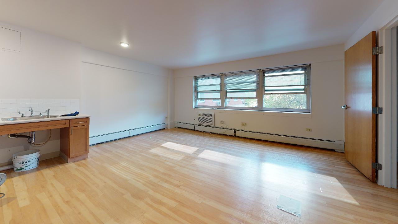 An empty living room with hardwood floors and a sink.
