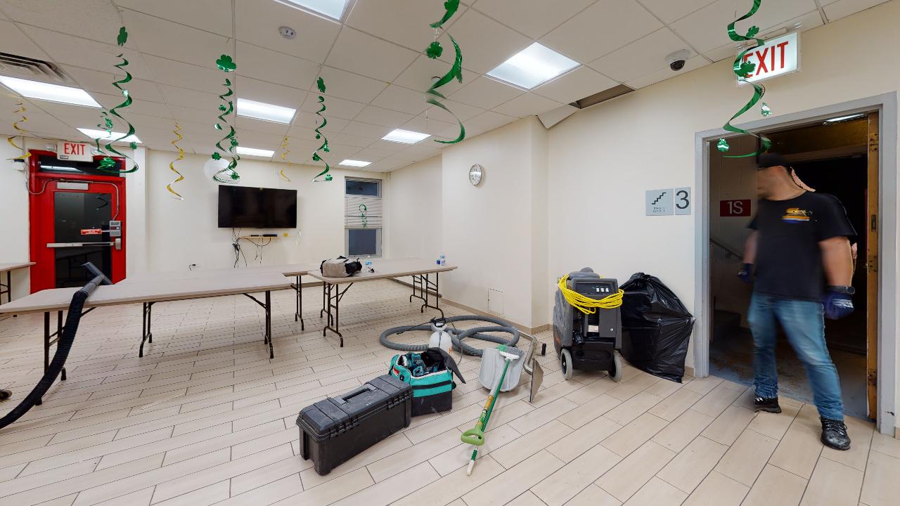 A man is standing in a room with tables and a vacuum cleaner.