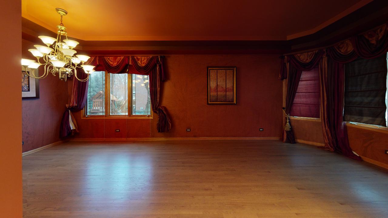 A large empty room with hardwood floors and a chandelier hanging from the ceiling.