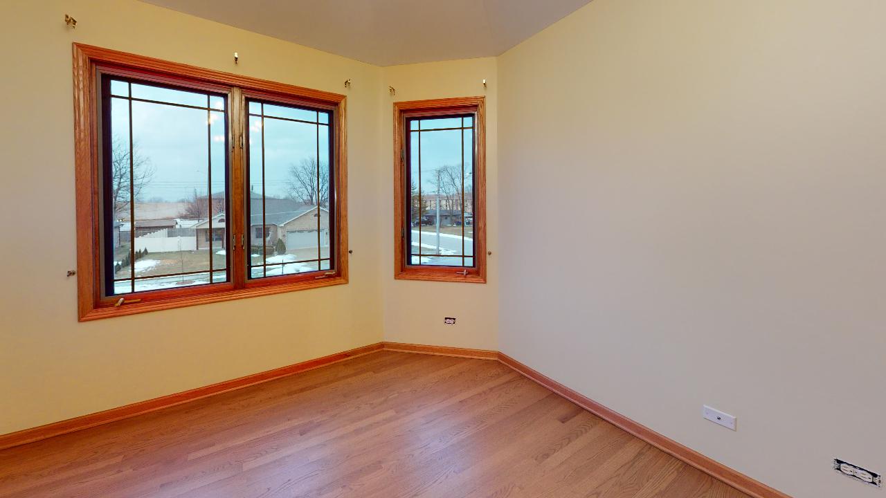 An empty room with hardwood floors and two windows.