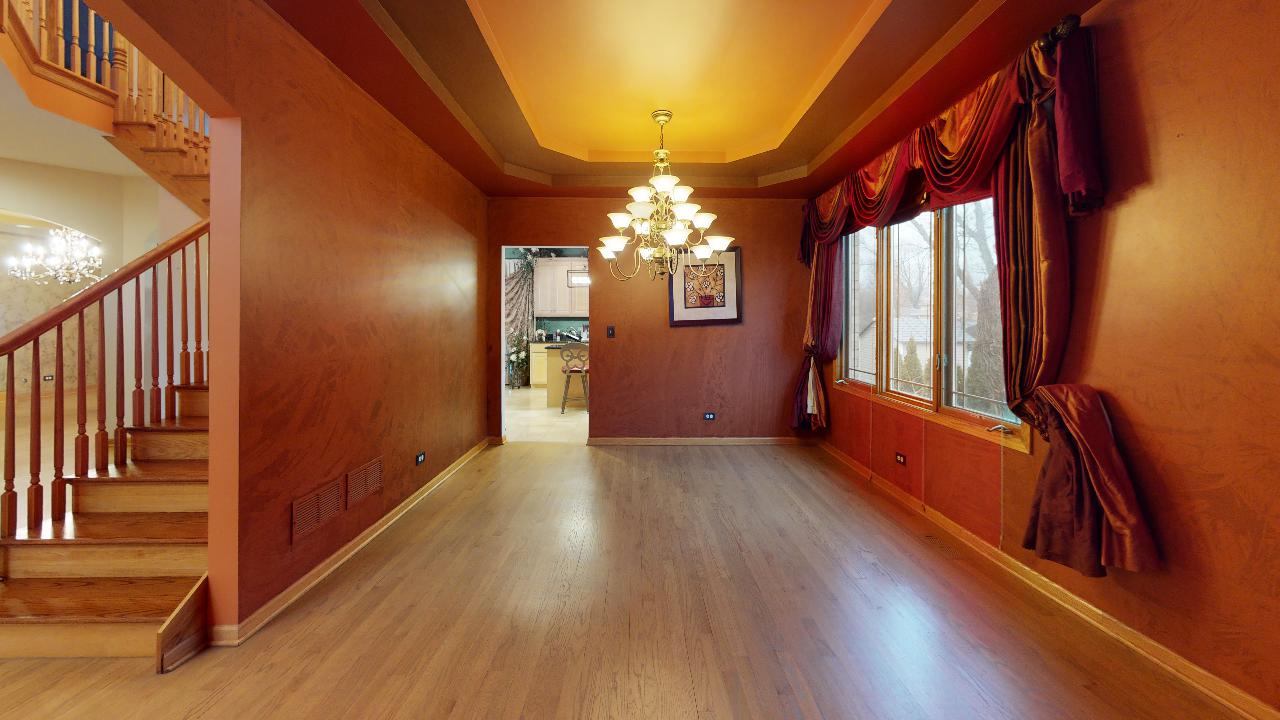 An empty living room with hardwood floors , red walls , stairs and a chandelier.