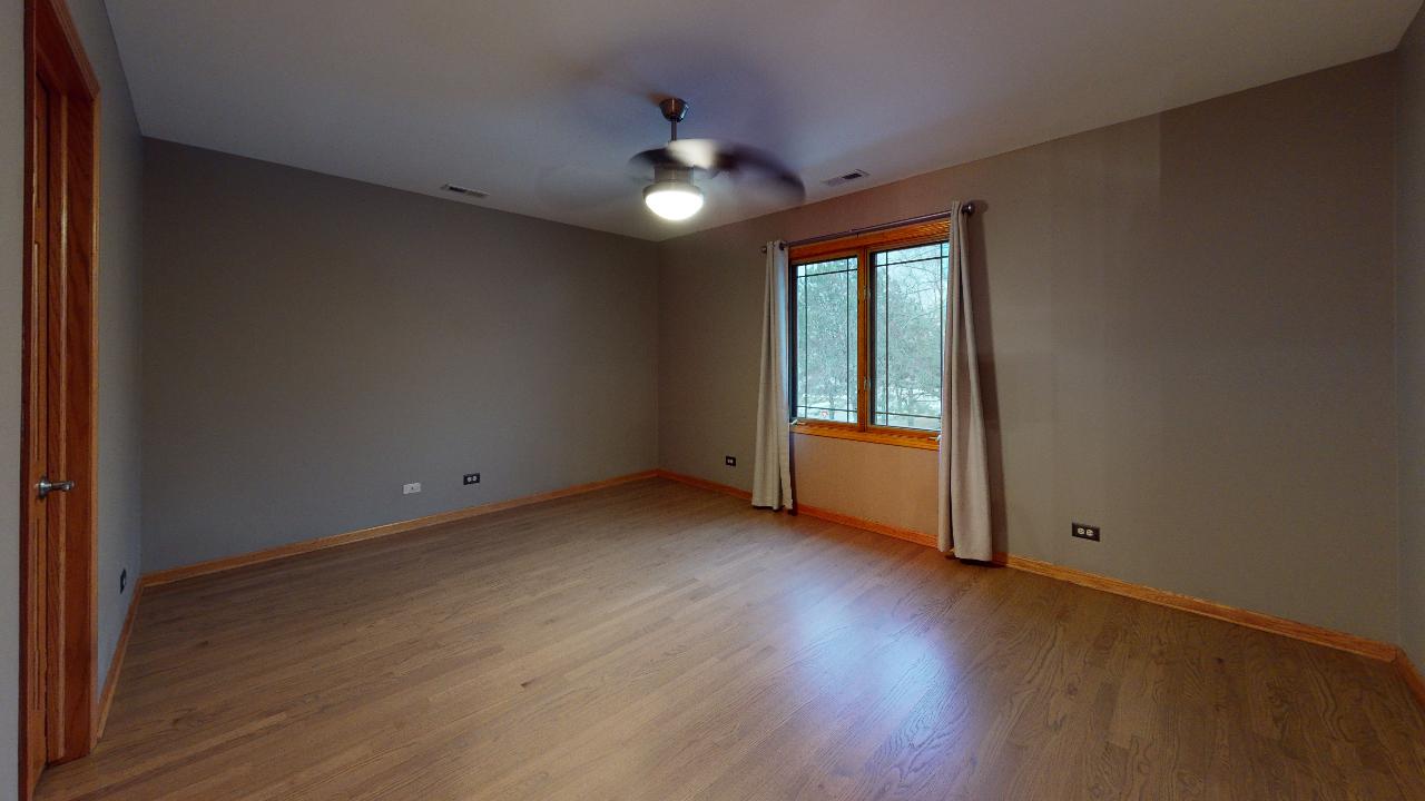 A large empty room with hardwood floors and a ceiling fan.