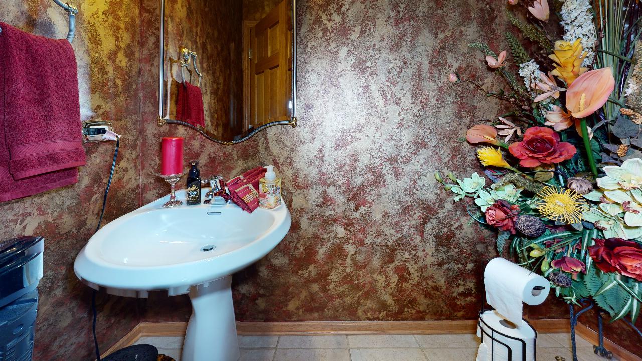 A bathroom with a sink , toilet , mirror and flowers on the wall.