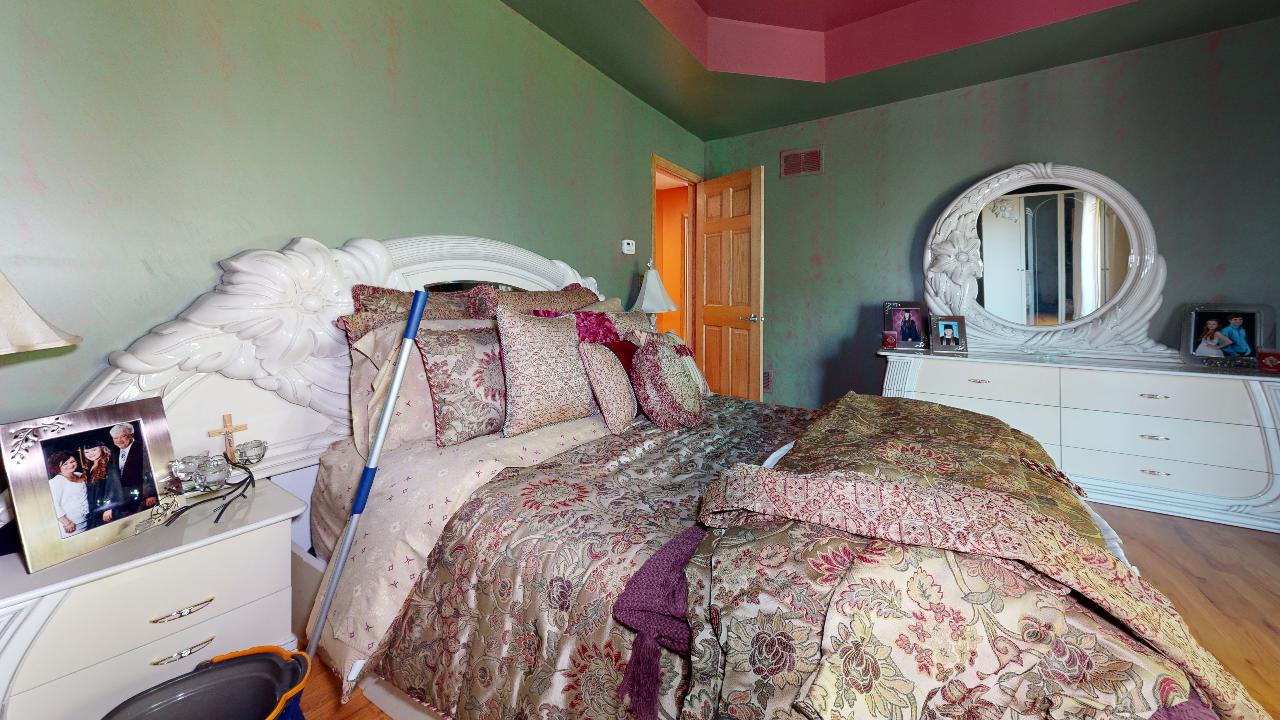 A bedroom with a bed , dresser , mirror and nightstand.