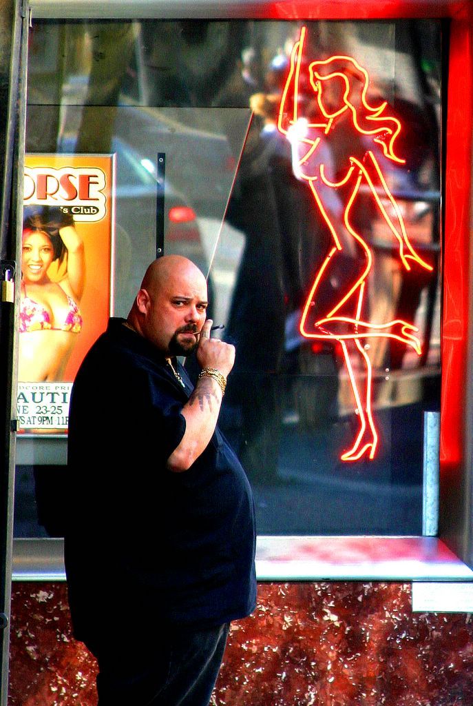 Man looking toward neon sign of woman in window.