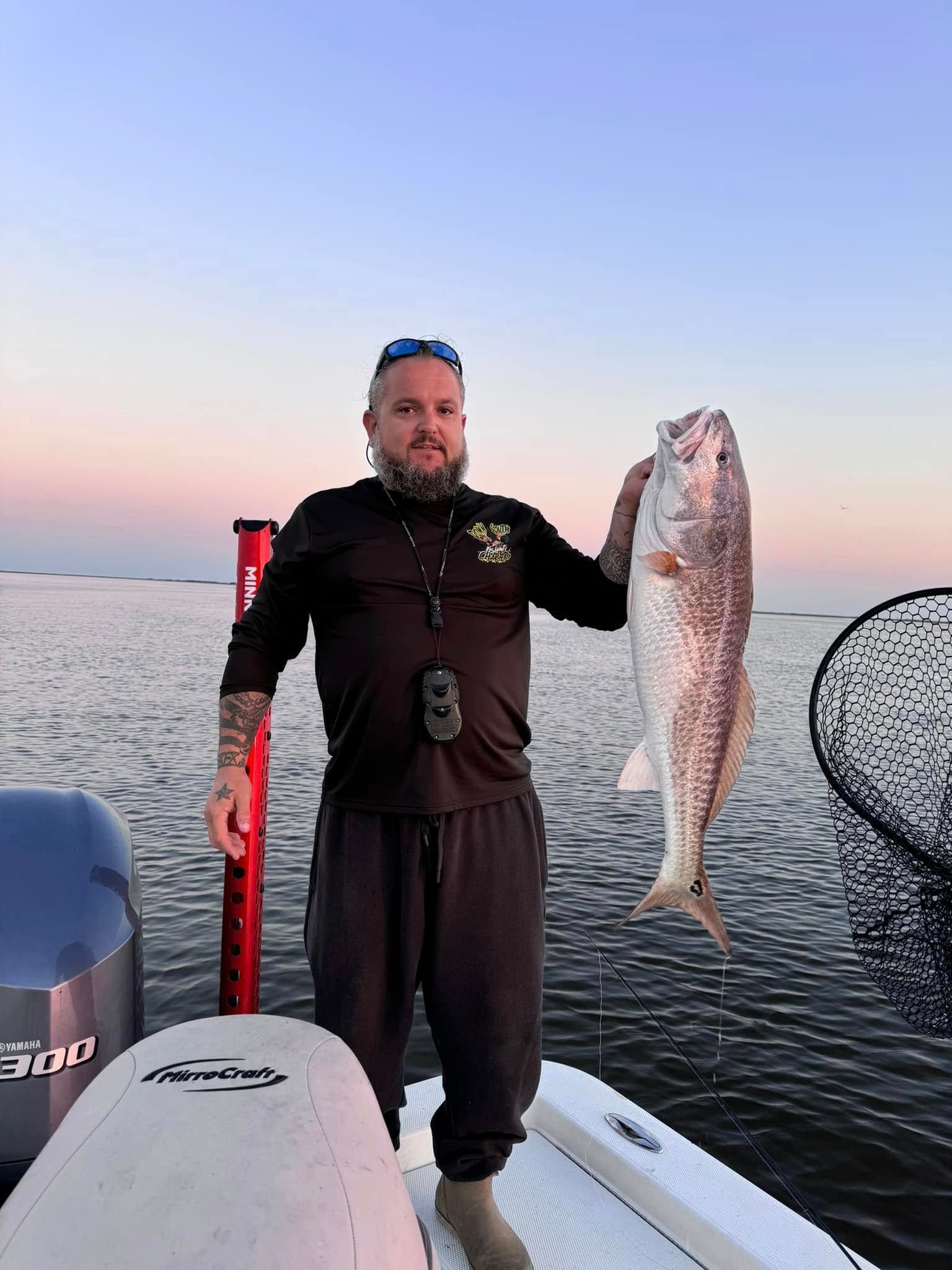 A man is standing on a boat holding a large fish.