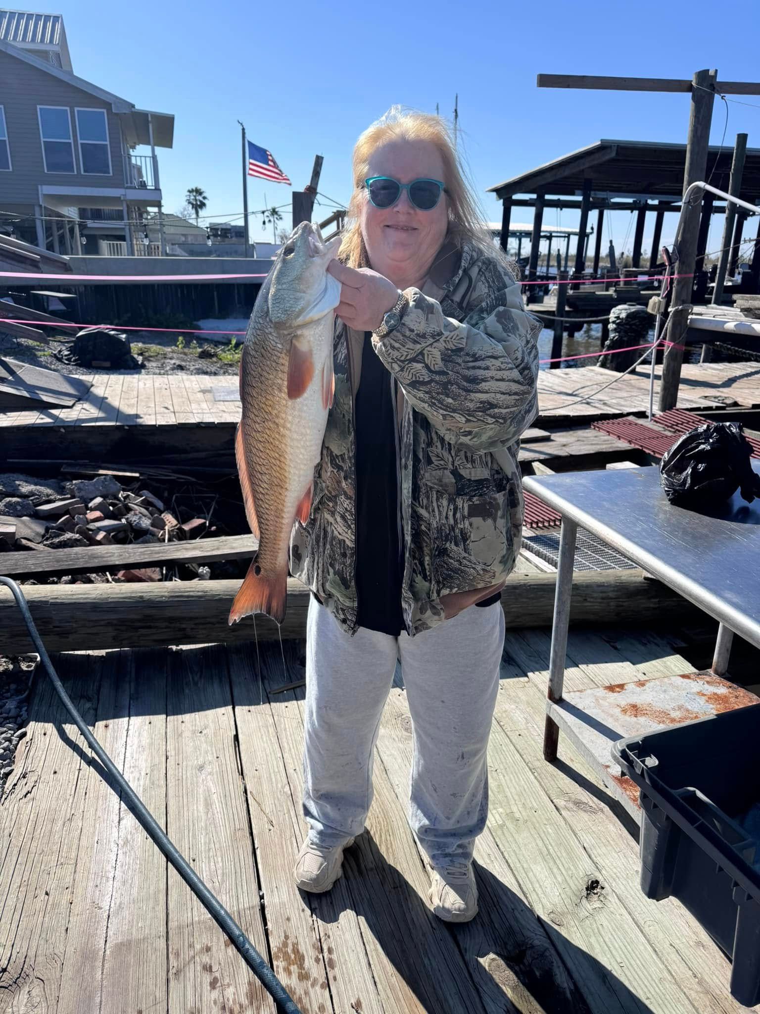 A woman is holding a large fish on a dock.