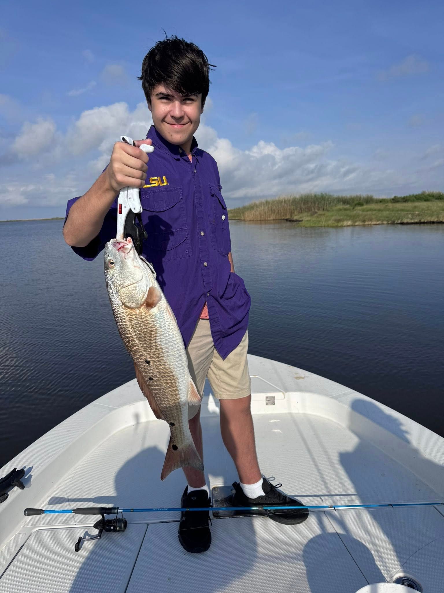 A young boy is holding a large fish on the back of a boat.