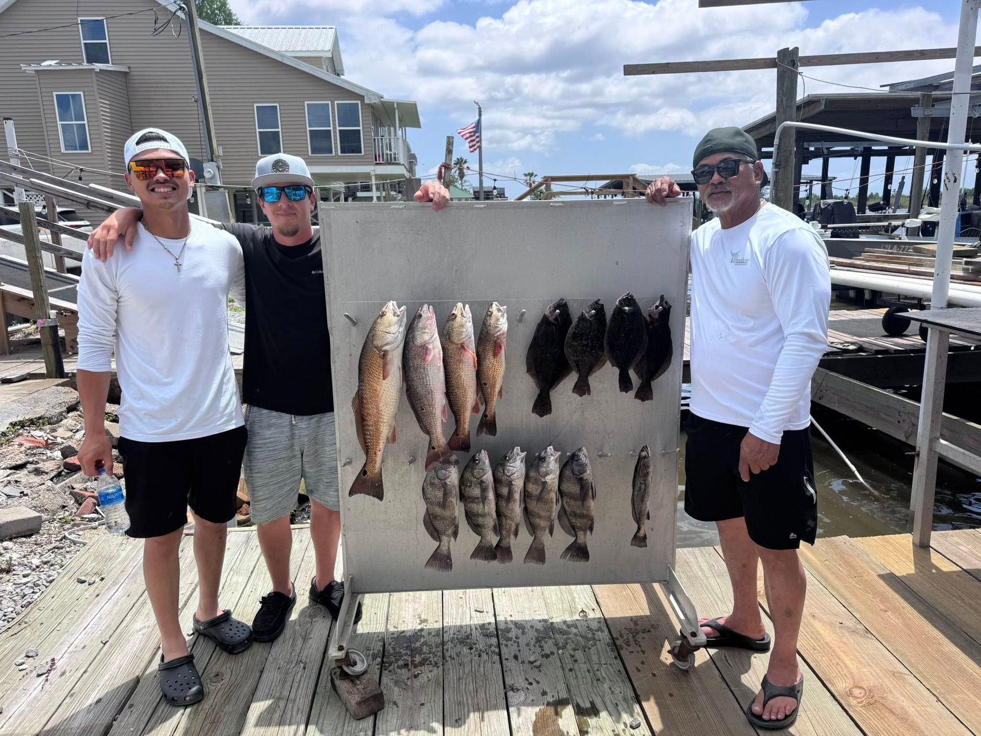 Three men are standing on a dock holding a sign with fish on it.