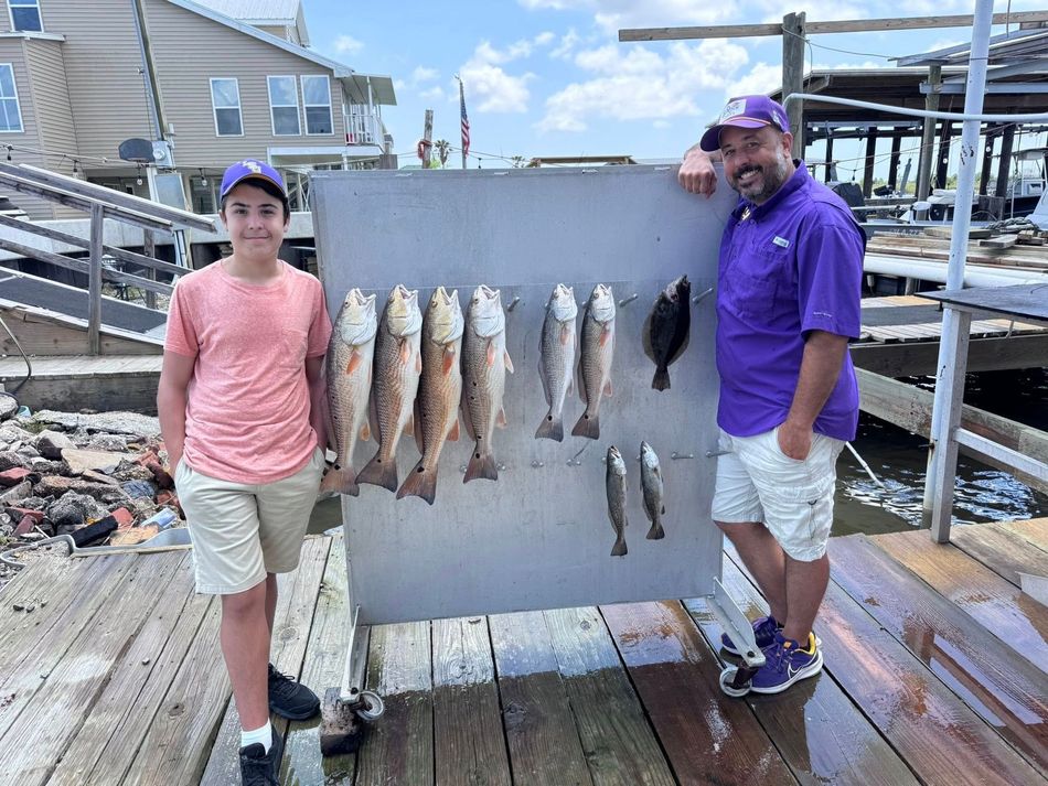 A man and a boy are standing on a dock holding a sign with fish on it.