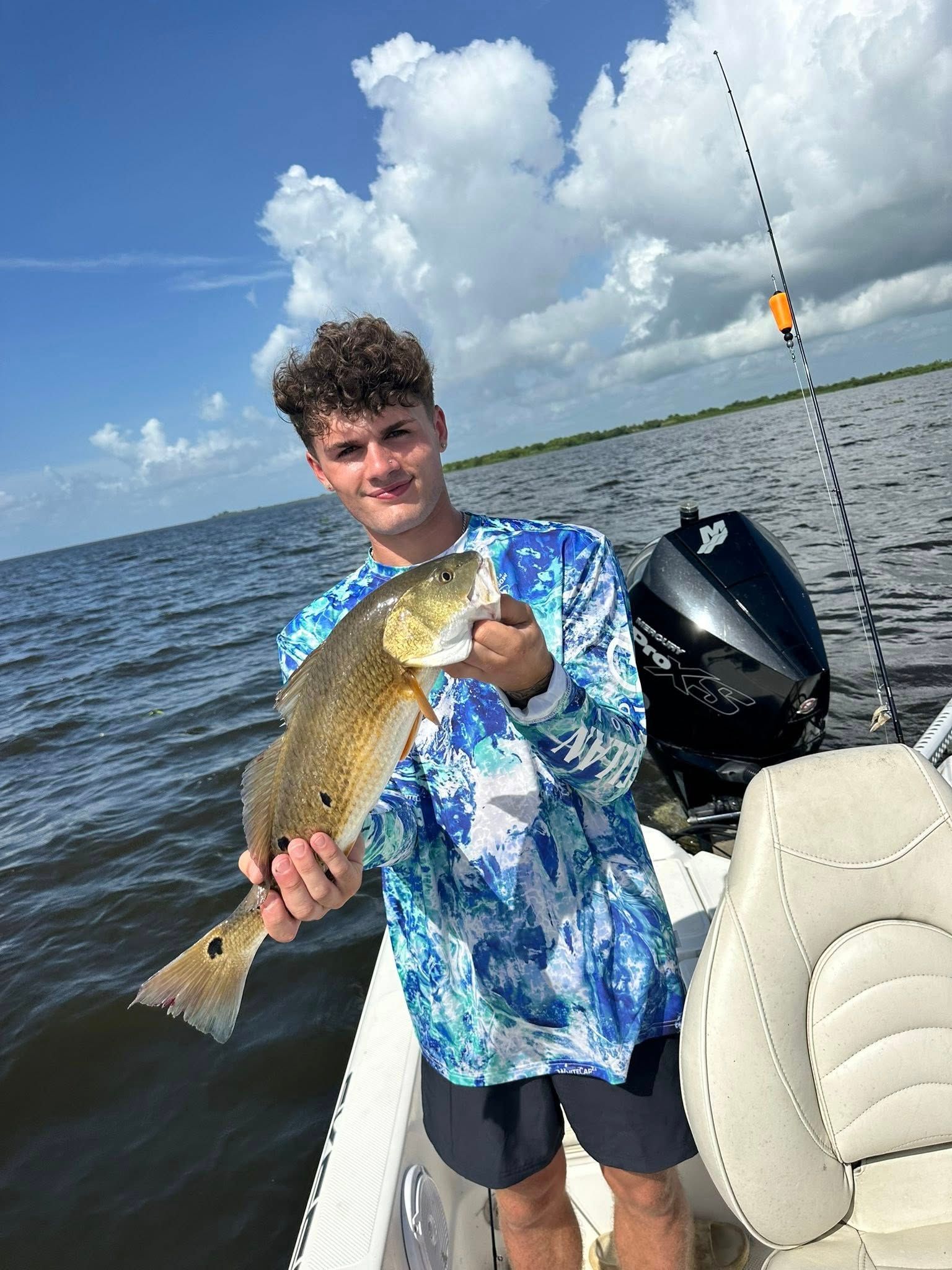 A young man is standing on a boat holding a large fish.