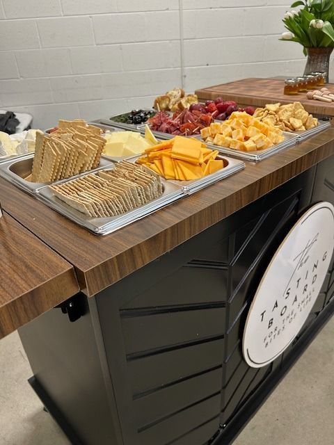 Cheese and cracker tasting board on black and wood cart; white wall background.