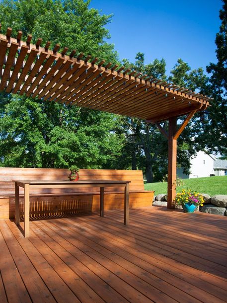 A wooden deck with a table and bench under a pergola.