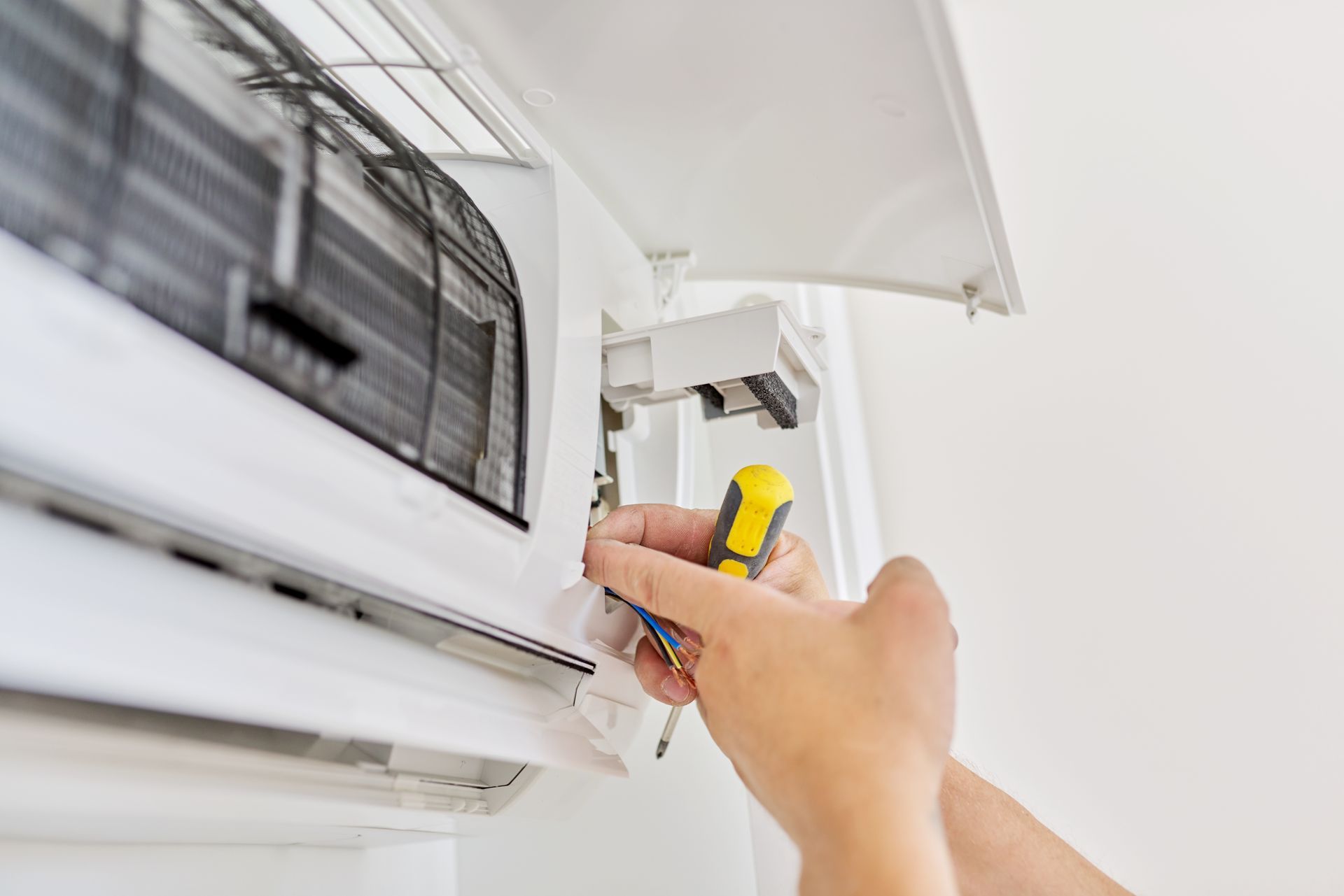 Servicing an air conditioner, close-up of a technician’s hand holding a screwdriver. Servicing an air conditioner, close-up of a technician’s hand holding a screwdriver.