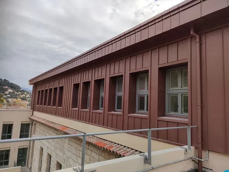 Façade en métal brun avec fenêtres, se détachant sur un ciel nuageux.