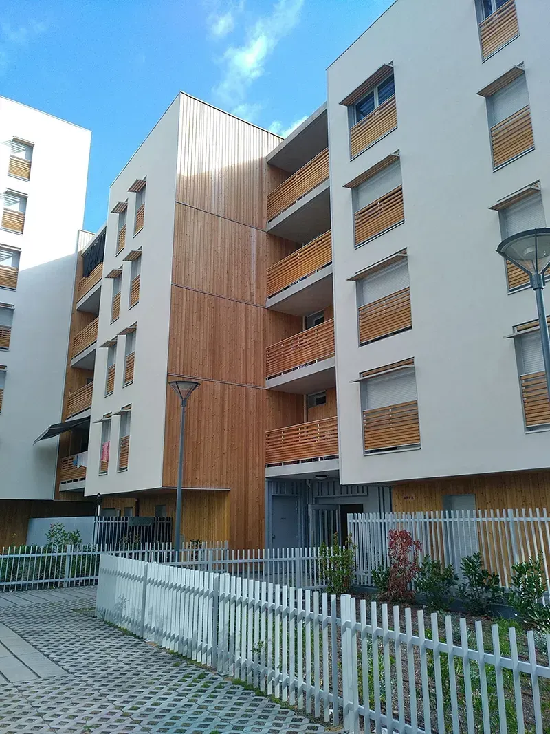 Immeuble d'appartements moderne avec lambris, balcons et façade claire, sous un ciel bleu.
