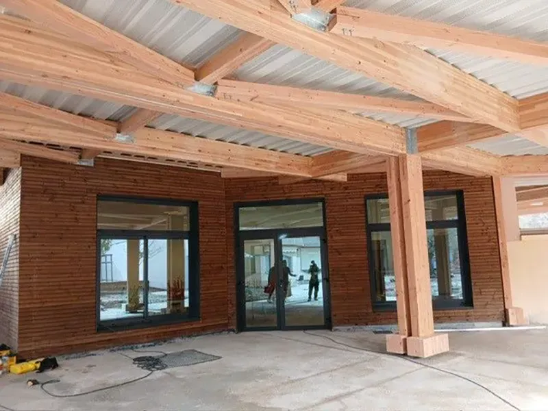 Extérieur en bois avec de grandes fenêtres, un porche couvert et des poutres apparentes.