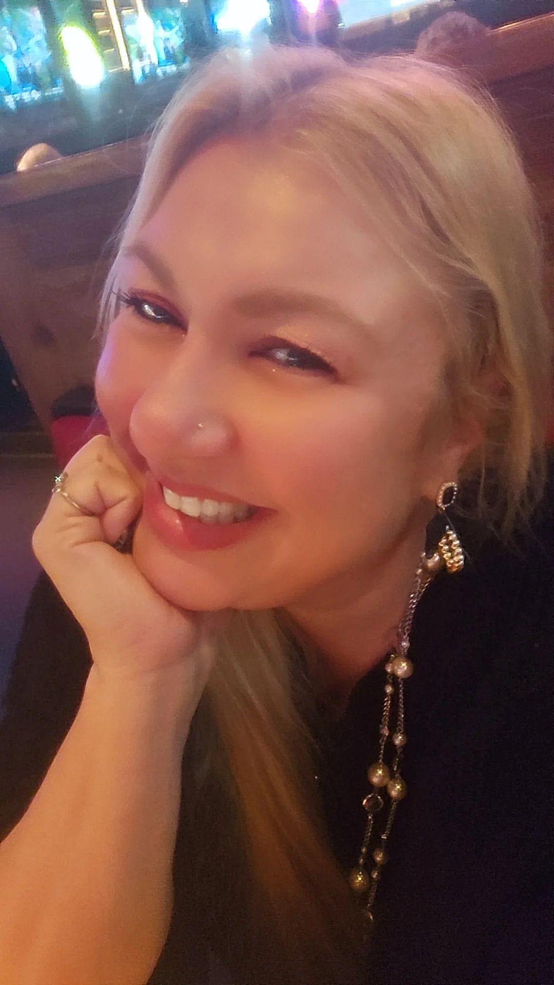Smiling blonde woman resting her chin on her hand in a dimly lit restaurant booth