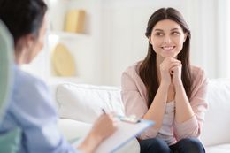Woman smiling during a therapy session, seated on a couch while speaking with a counselor.